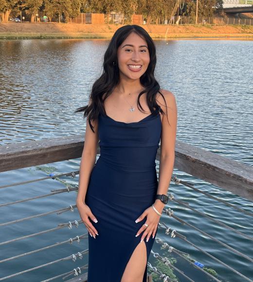 Young woman with dark hair in navy dress, standing on a lakeside wooden dock at sunset